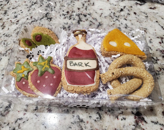 Multiple dog treats in shapes of strawberries, olives, cheese, pretzels, and wine bottle.