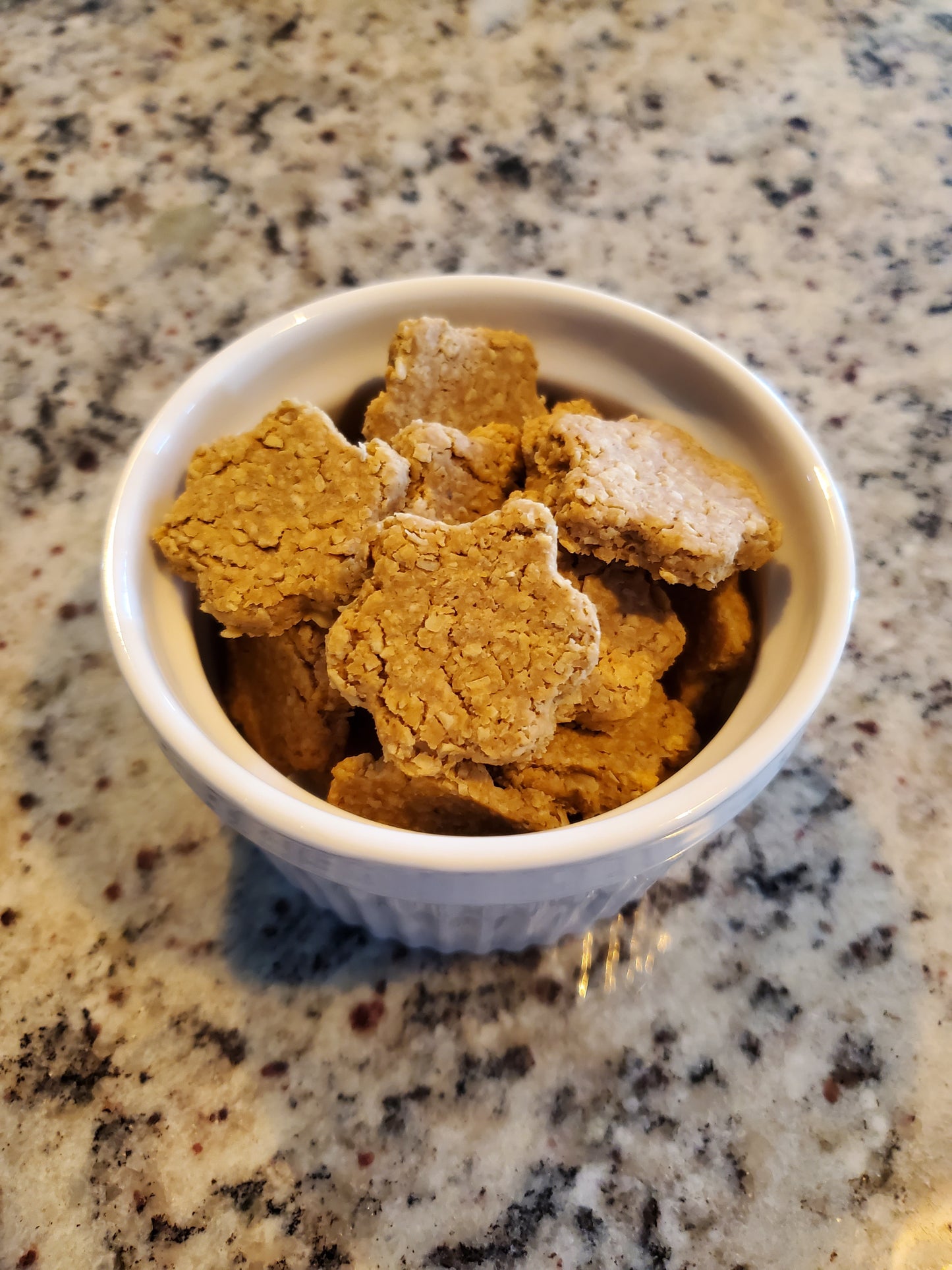 Paw print shaped dog treats in white bowl on granite counter