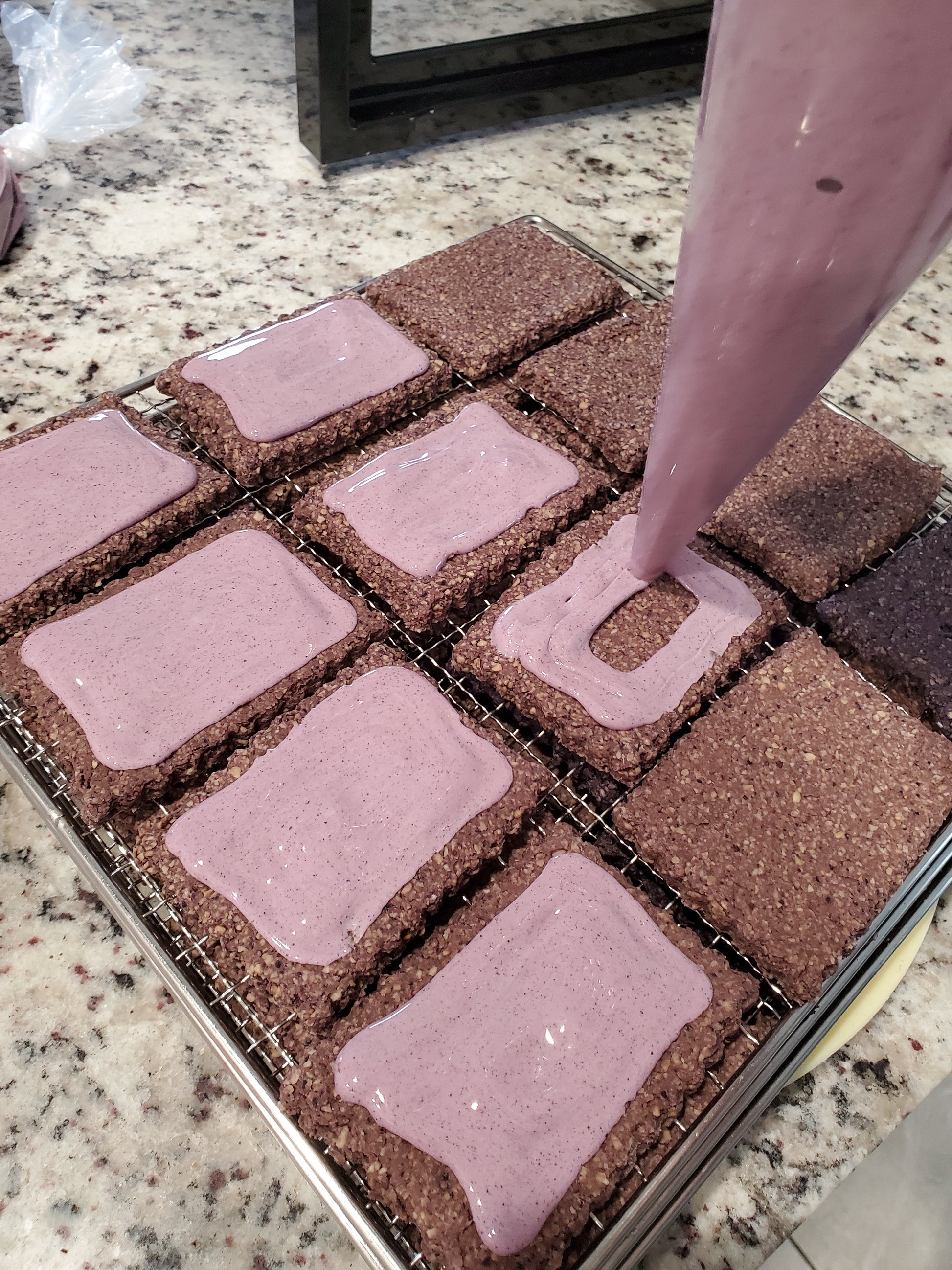 Multiple blueberry puptarts on cooling rack being iced with purple icing