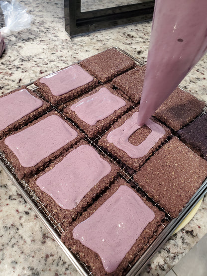 Multiple blueberry puptarts on cooling rack being iced with purple icing