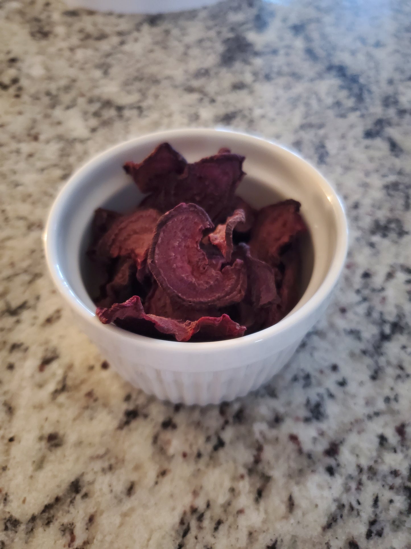 White bowl filled with dried purple beet chips on a granite countertop