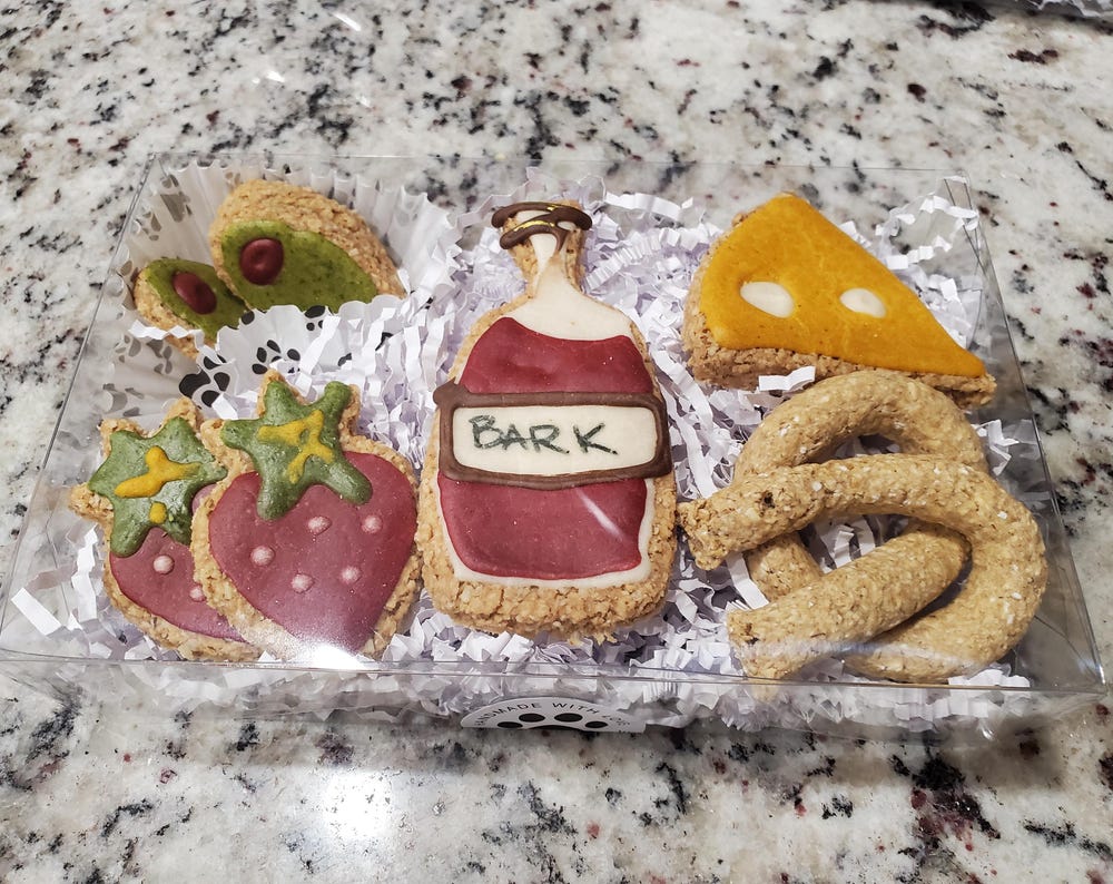 Multiple dog treats in shapes of strawberries, olives, cheese, pretzels, and wine bottle. 