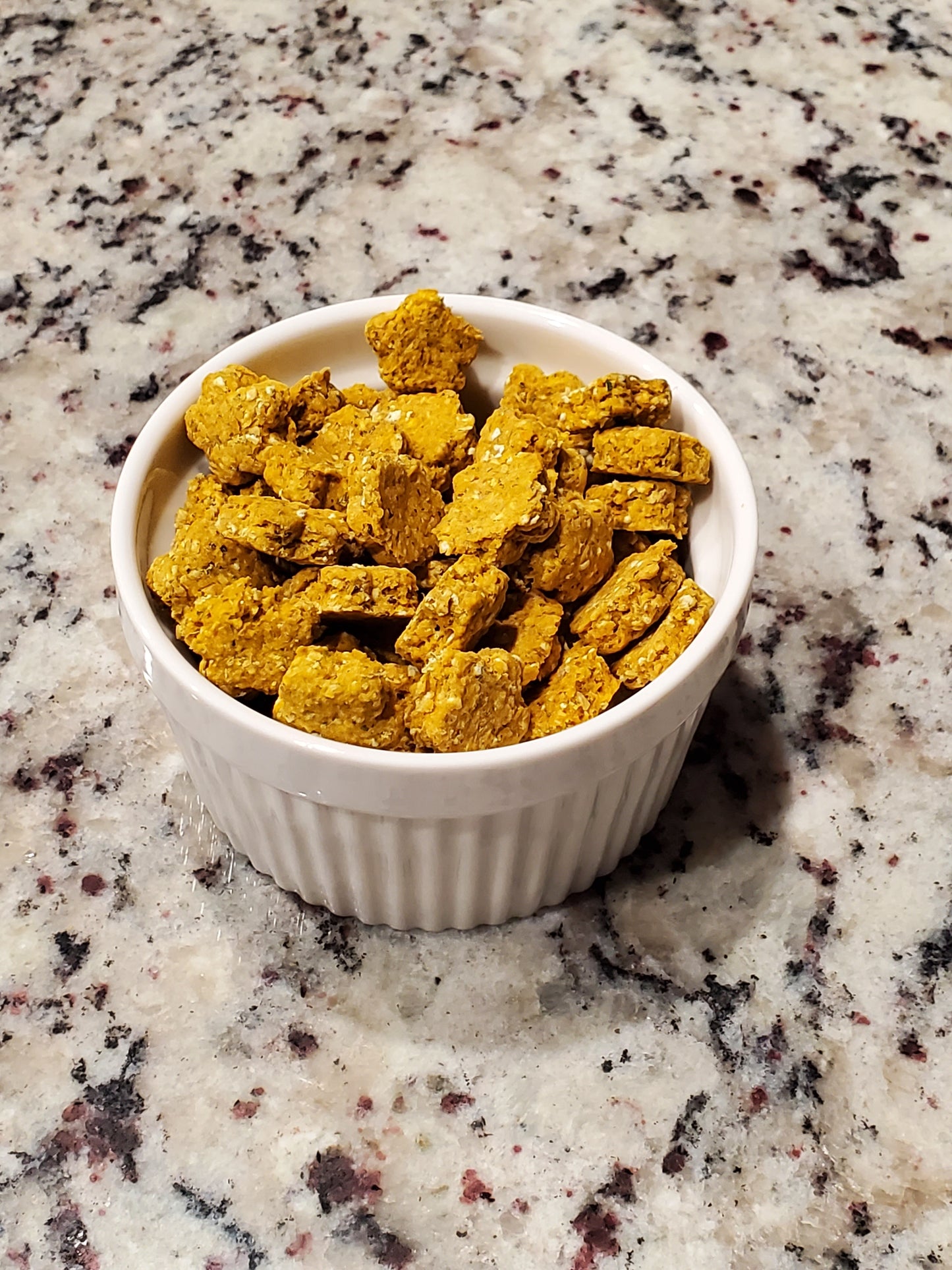 White bowl filled with yellow cat treats on a speckled countertop