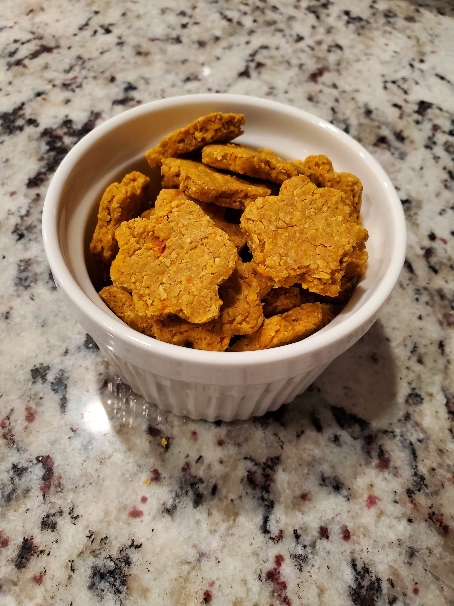 Star-shaped dog treats in a white bowl on a speckled countertop